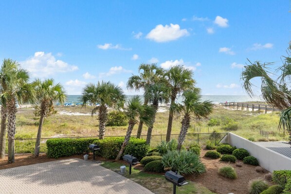 A patio area with a view of the beach, palm trees, and a fence. - Phoenix East 101 (Orange Beach)