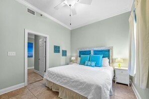 A bedroom with a bed, a nightstand, a ceiling fan, and a door leading to another room. - Phoenix East 101 (Orange Beach)