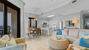 Amplia sala de estar con sofá, mesa de centro y comedor. Se ve una cocina al fondo con electrodomésticos modernos.
