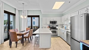 Una cocina moderna con armarios blancos, una isla central, electrodomésticos de acero inoxidable y un comedor con sillas de mimbre.