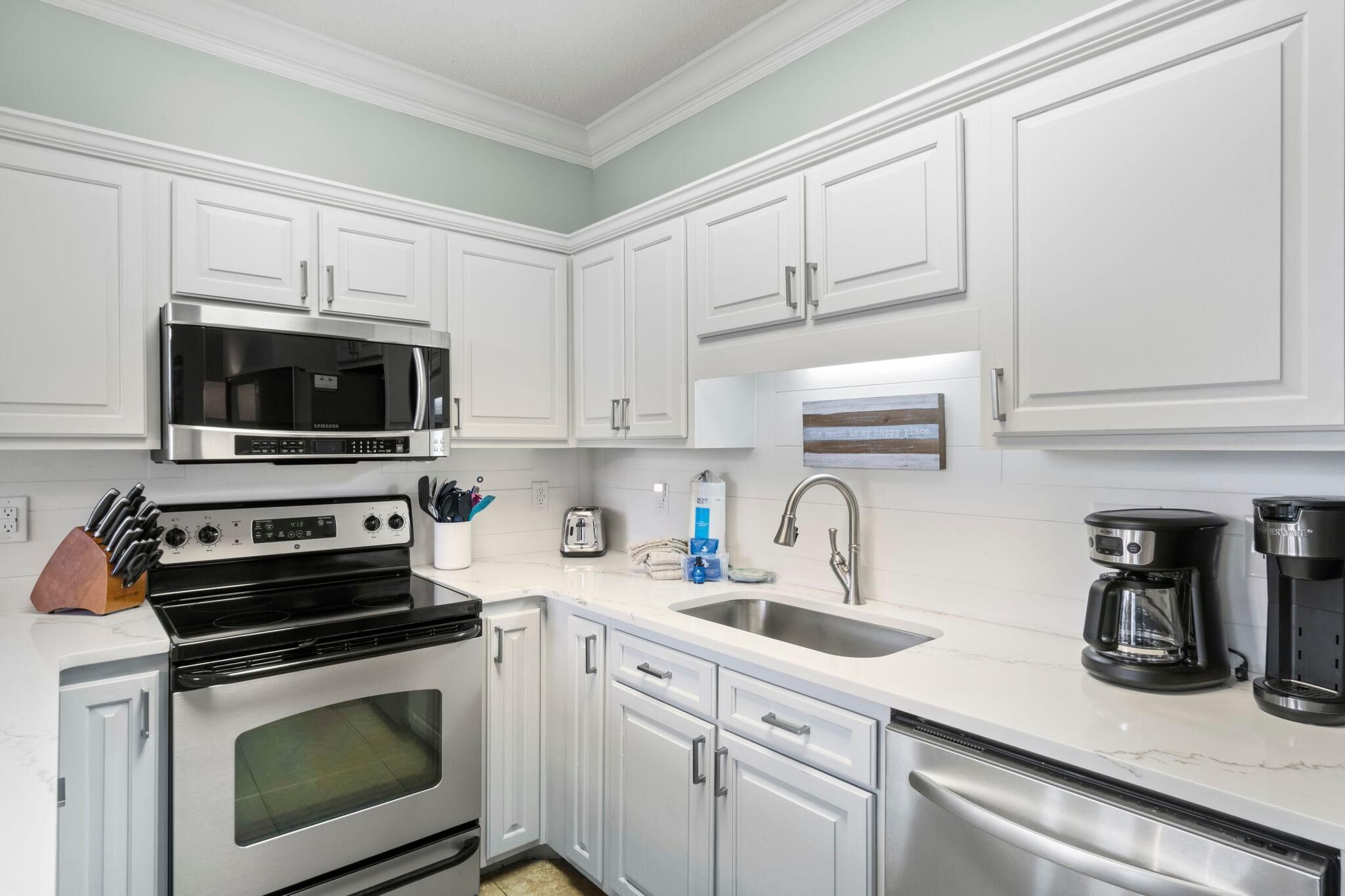 A modern kitchen with white cabinets, stainless steel appliances, a double oven, a microwave, a toaster, and a coffee maker.
