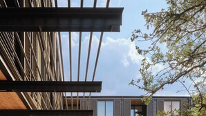 An outdoor patio area with stone flooring, metal chairs, and umbrellas, adjacent to a modern building with large windows and a wooden pergola. - The Inn at Green Pastures (Austin)