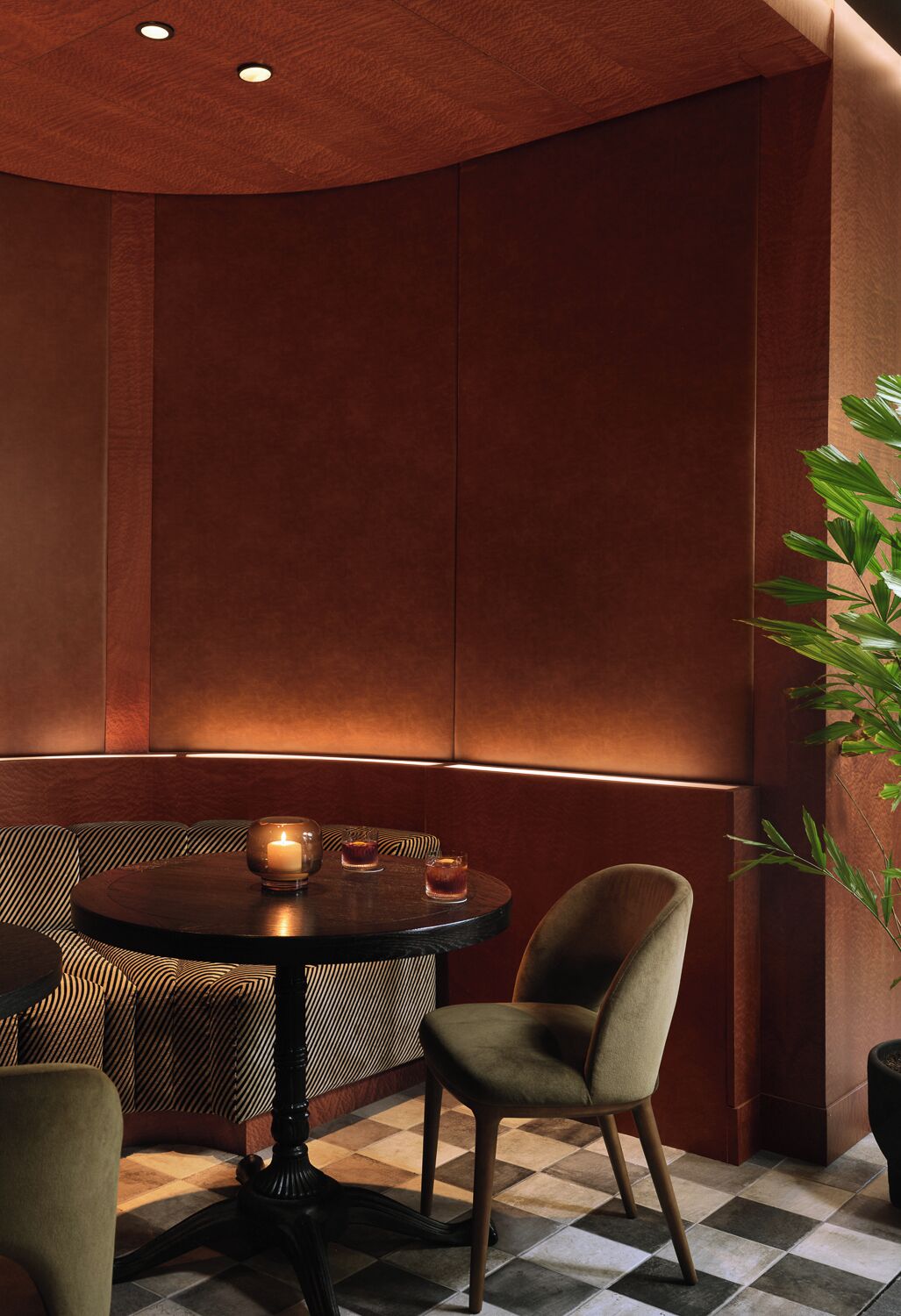 A corner of a room with a round table, two chairs, a candle, and a plant.