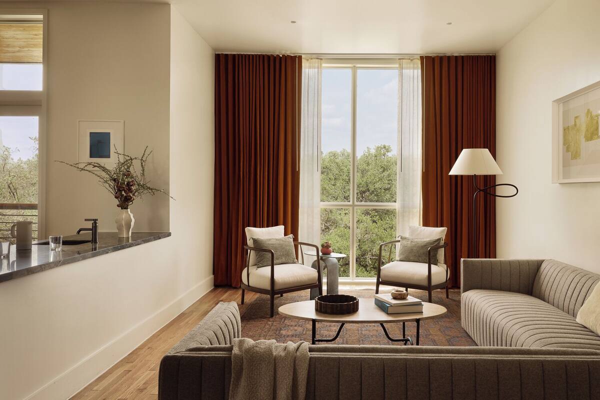 Un salon moderne avec un canapé, des fauteuils, une table basse et une vue dégagée grâce à de grandes fenêtres.