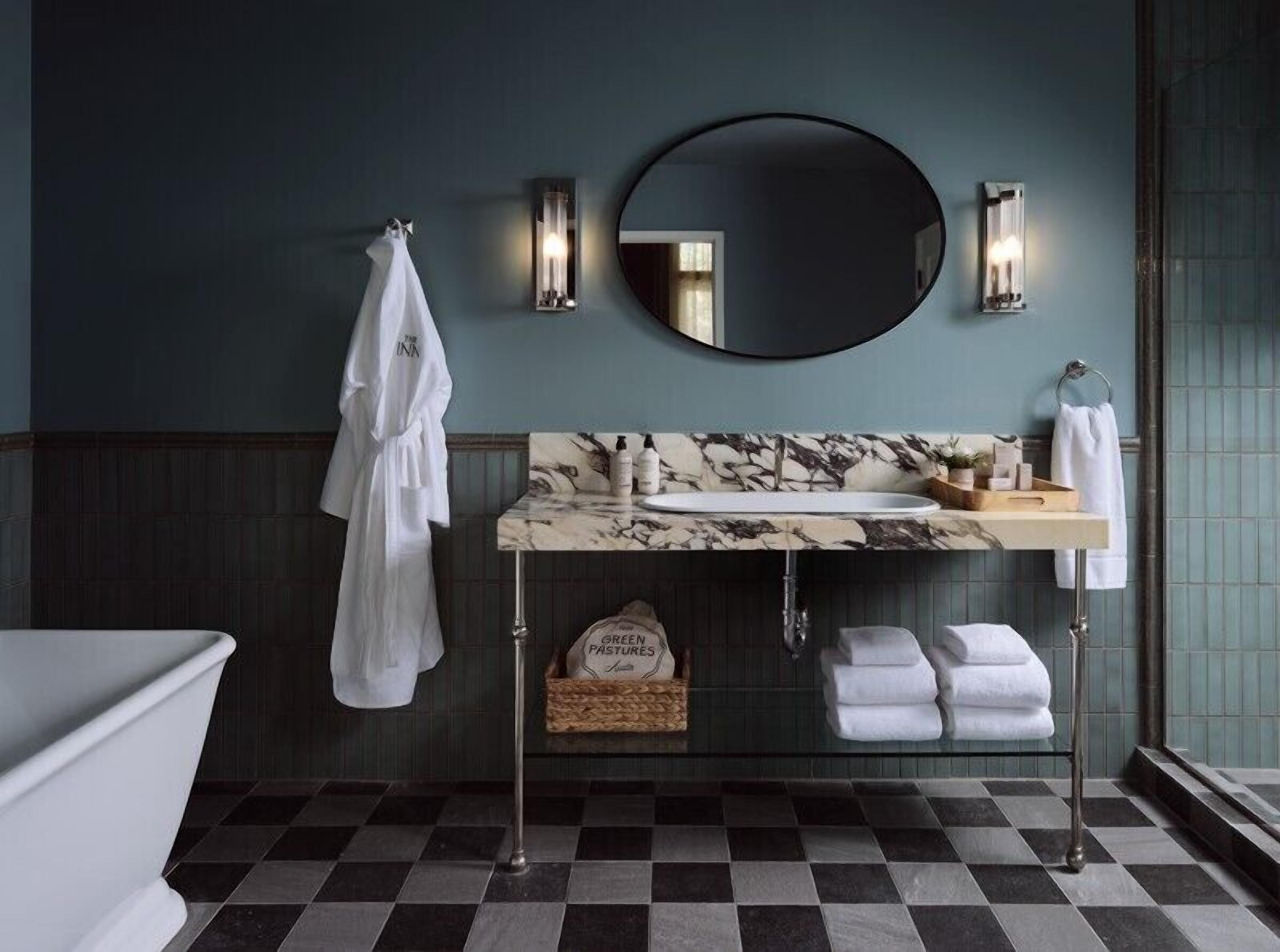 A bathroom with a marble sink, a round mirror, and a towel rack.