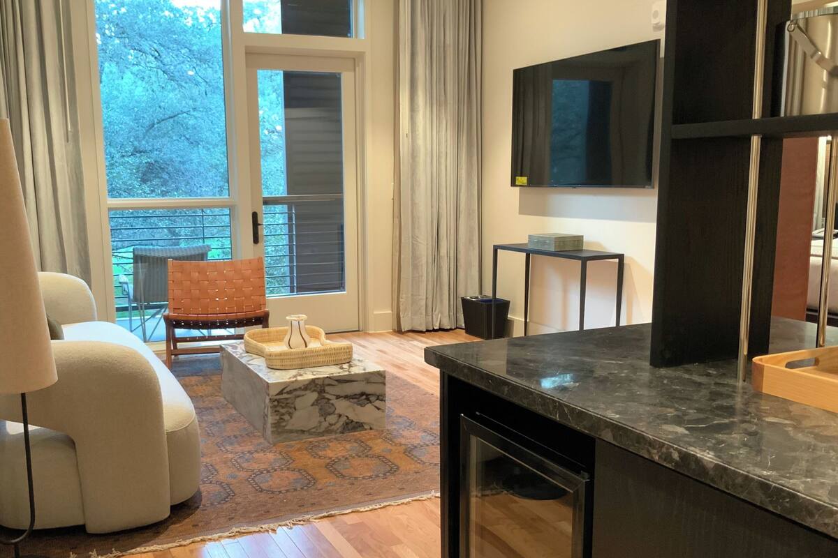 Un salon moderne avec un canapé, une table basse, un téléviseur et un balcon offrant une vue sur les arbres.