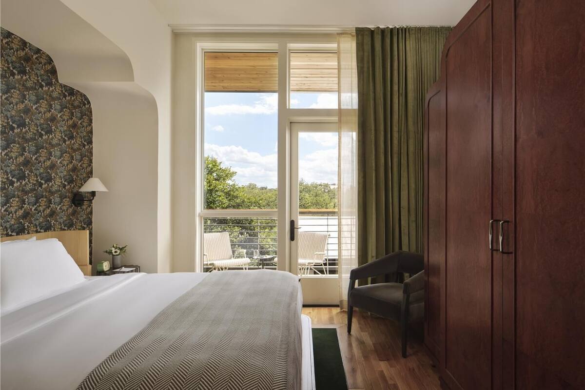 Une chambre d’hôtel avec un lit, une chaise, une armoire et un balcon offrant une vue.