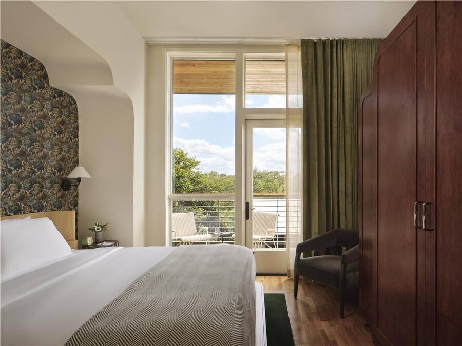 A hotel room with a bed, a chair, a wardrobe, and a balcony with a view.