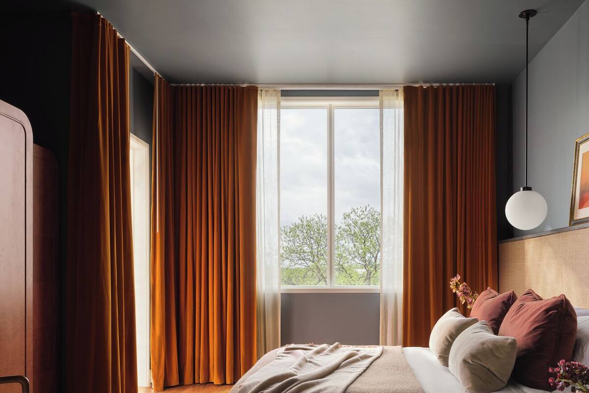 Une chambre à coucher comprenant un lit, une chaise, une table de chevet et une fenêtre avec des rideaux.