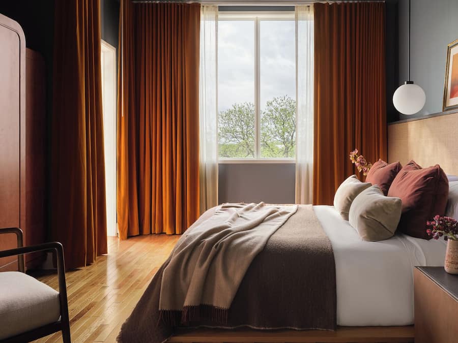 A bedroom with a bed, a chair, a bedside table, and a window with curtains.