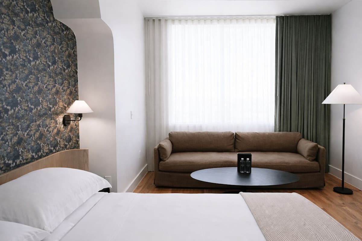 Une chambre d’hôtel avec un lit, un canapé, une table basse ronde et deux lampes.