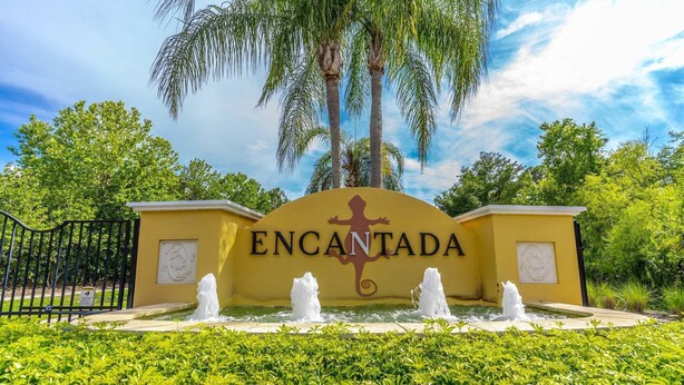 Une enseigne avec le mot «ENCANTADA» et un logo représentant un lézard, le tout entouré d’une fontaine et de verdure.