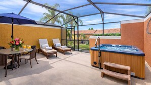 Un espace extérieur abrité, aménagé avec des chaises longues, un jacuzzi et une table où sont disposées des boissons et des fleurs.