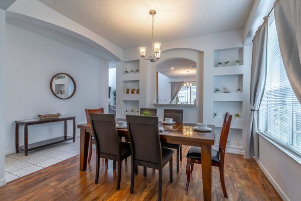 A dining area with a wooden table and chairs, a chandelier, and built-in shelving with decorative items.