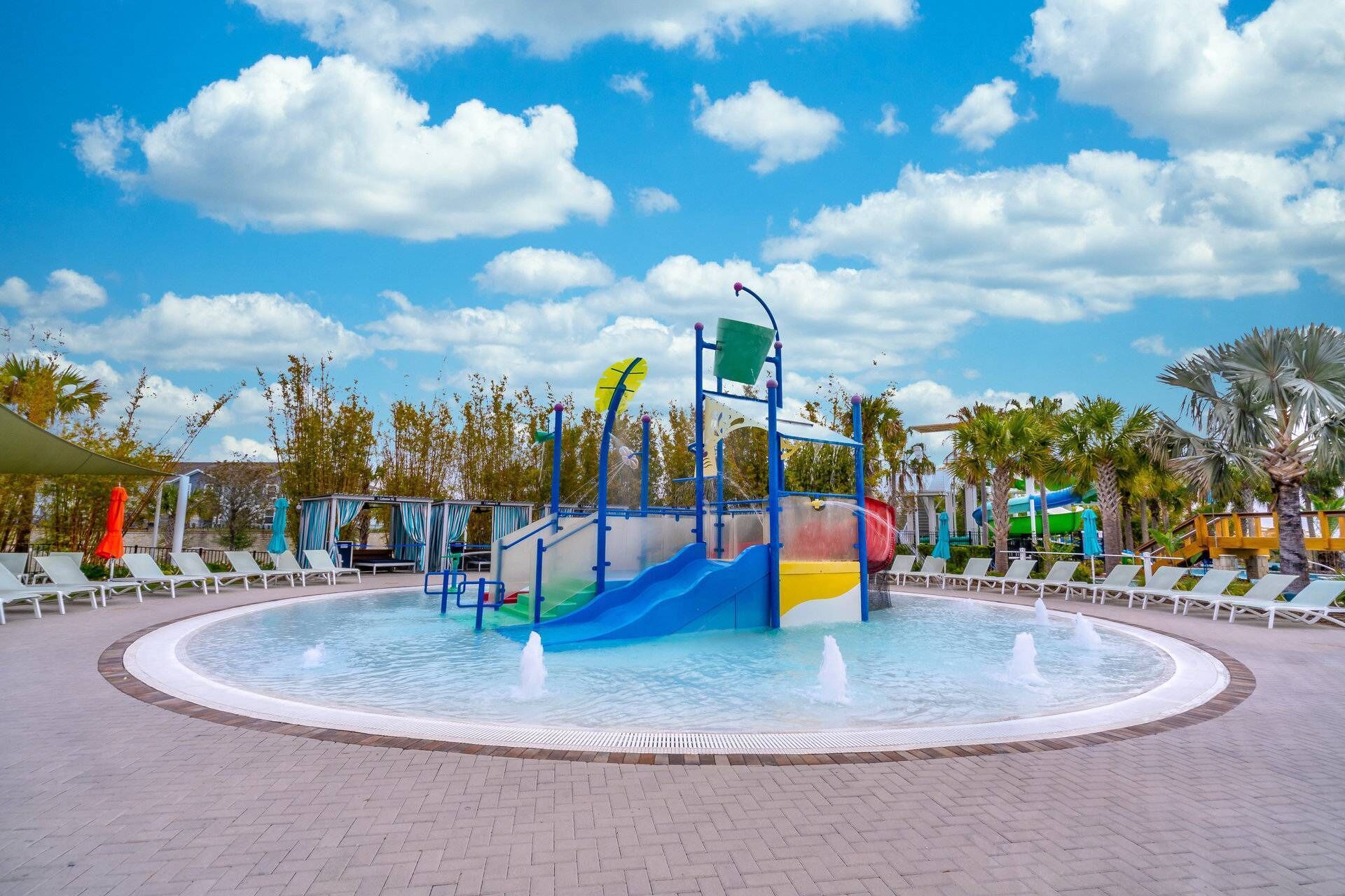 Ein Wasserspielbereich mit Rutschen und einer zentralen Fontäne, umgeben von Liegestühlen und Palmen.