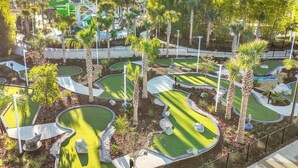 Een midgetgolfbaan met meerdere holes, palmbomen en een waterglijbaan op de achtergrond.