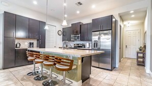 A modern kitchen with dark cabinets, stainless steel appliances, a central island with bar stools, and pendant lighting. - 417 Festival (Davenport)
