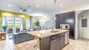 A modern kitchen with dark cabinets, a central island, and a dining area with a gray sofa. - 417 Festival (Davenport)