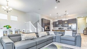 A modern living room with a grey sectional sofa, a staircase, and a kitchen in the background. - 417 Festival (Davenport)