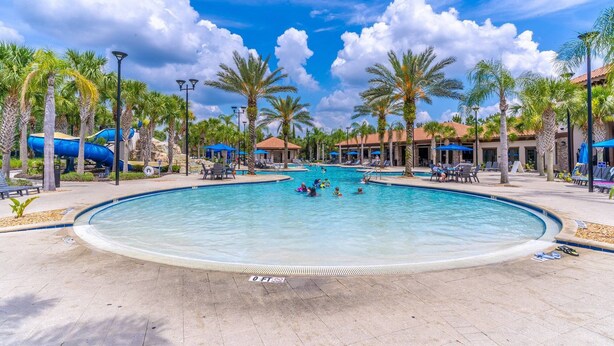 A large outdoor swimming pool surrounded by palm trees and lounge chairs, with a clear blue sky above. - 4763 Solterra (Davenport)