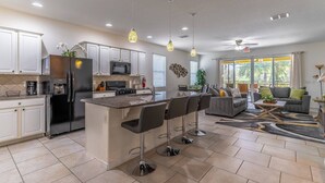 A modern kitchen with white cabinets, a black refrigerator, and a central island with bar stools. - 4763 Solterra (Davenport)