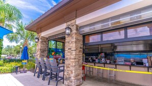 An outdoor seating area with stone pillars, a covered patio, and a bar with a caution tape barrier. - 4763 Solterra (Davenport)