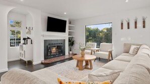 Un salon moderne avec une cheminée, des meubles blancs et une grande fenêtre donnant sur l’extérieur.