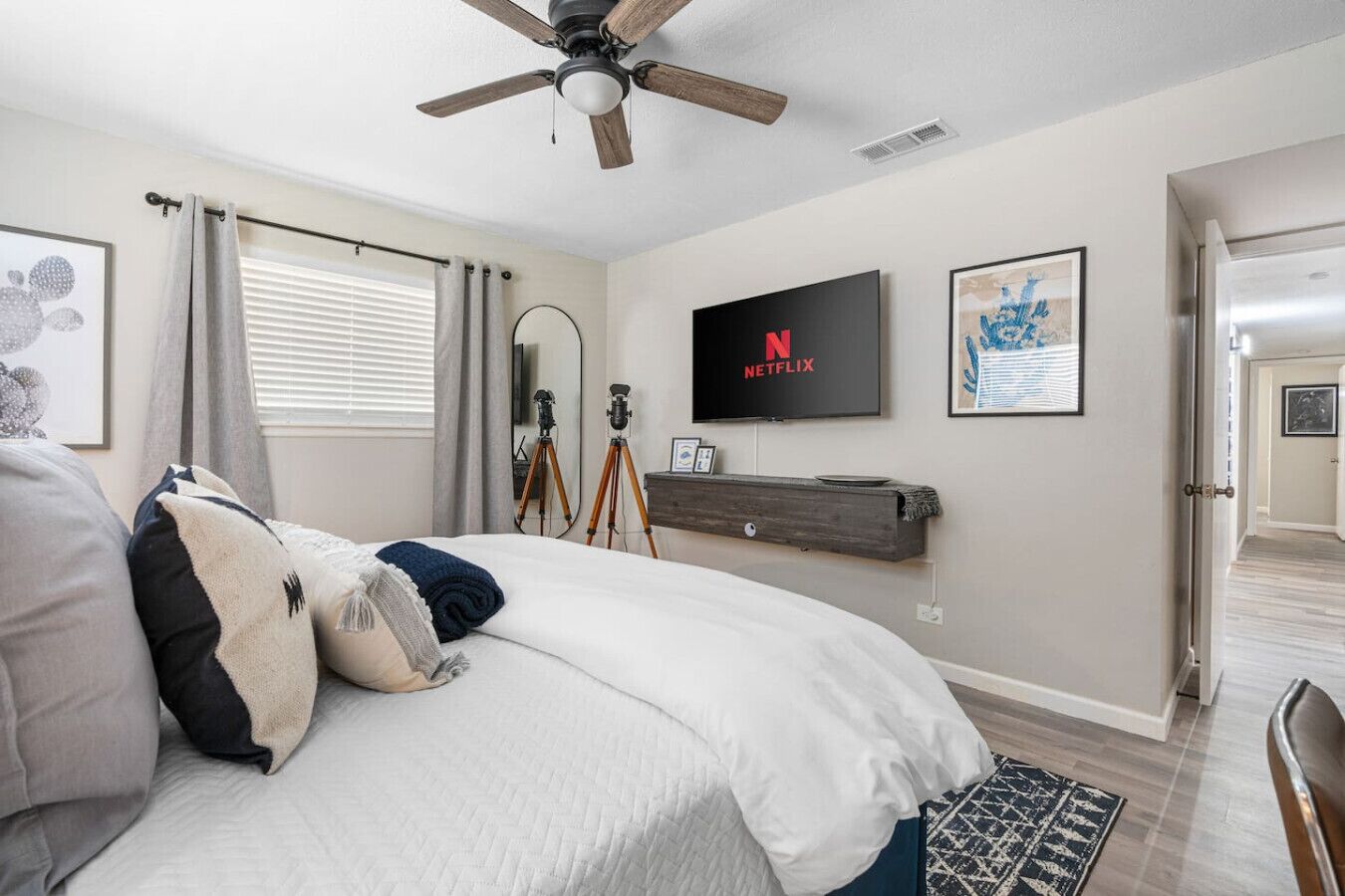 Un dormitorio con una cama, ventilador de techo, televisor montado y un trípode.