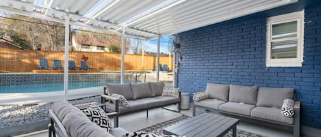A covered patio area with a pool, outdoor furniture, and a blue brick wall.
