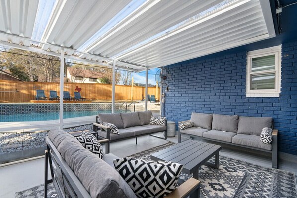 A covered patio area with a pool, outdoor furniture, and a blue brick wall.