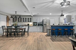 A modern kitchen with white cabinets, a blue island, bar stools, and pendant lighting.