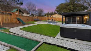 A backyard with a hot tub, a wooden swing set, and a grassy area. - Central Loc~Stylish~Pool~HotTub (San Antonio)