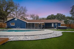 A backyard with a swimming pool, a hot tub, and a covered patio area.
