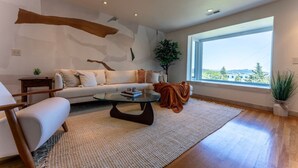 A modern living room with a sofa, coffee table, and a large window offering a view of the outdoors.