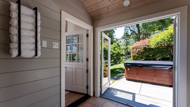 A hallway with a towel rack, a door leading to a garage, and a view of a backyard with a hot tub.