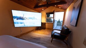 A hotel room with a large bed, a TV mounted on the wall, a chair, and a balcony with a view.