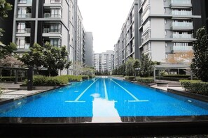 Un edificio residencial moderno con piscina central, rodeado de vegetación y otros edificios.