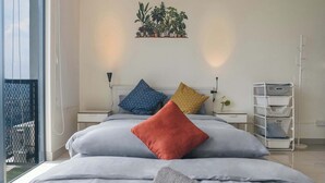 Ein Schlafzimmer mit einem Bett, Kissen, einem Deckenventilator, einem Nachttisch, einer Wandpflanze und einem Fenster mit Blick.