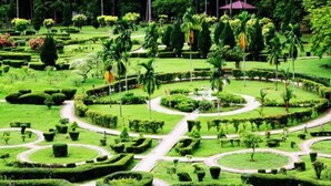 Ein sorgfältig angelegter Garten mit kreisförmigen Wegen, geometrisch geschnittenen Hecken und verschiedenen Bäumen.