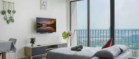 A modern bedroom with a large bed, a TV mounted on the wall, and a balcony with a city view.