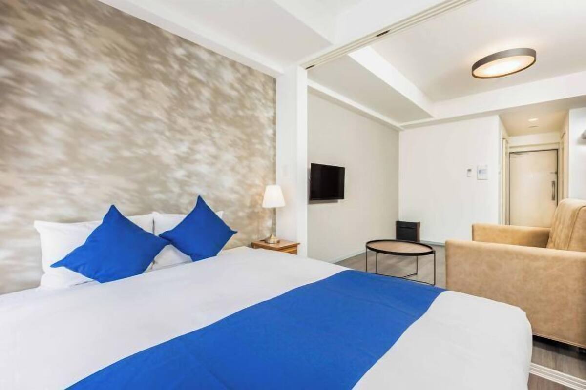 A hotel room with a bed, a sofa, a small table, and a TV.