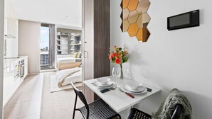 A modern hotel room with a dining area, a large window, and a view of the city. - Cozy Studio Near Southern Cross With City Views (Melbourne)