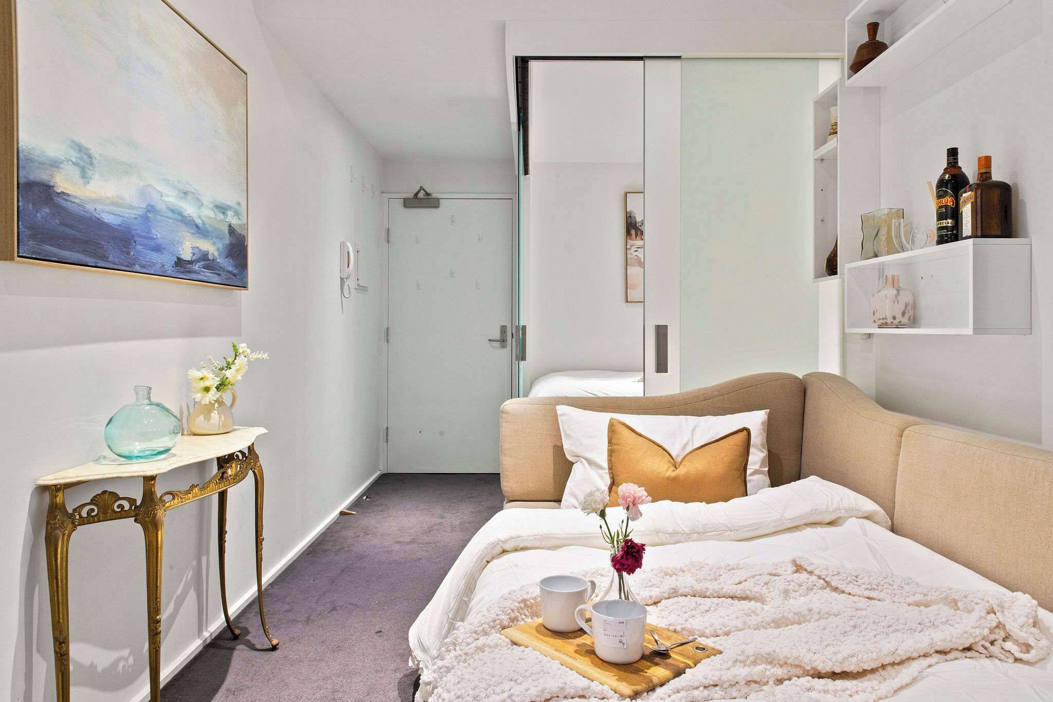 A neatly arranged bedroom with a bed, bedside table, and a wall-mounted shelf with decorative items.