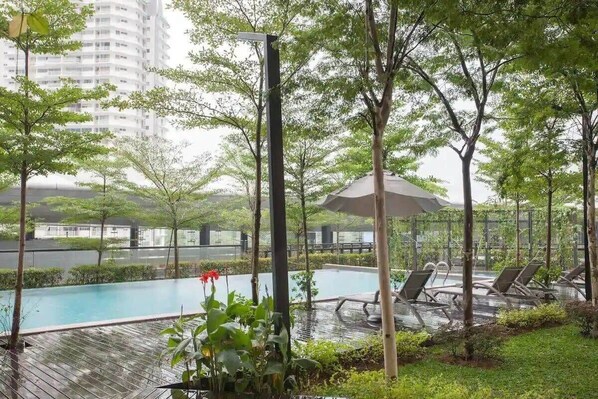Un espace piscine aménagé sur le toit, avec des chaises longues et des parasols, entouré d’arbres et de verdure.