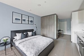 A modern bedroom with a large bed, a bedside table with a lamp, and a view into the adjacent kitchen. - A Stylish Studio Right Next to Southern Cross (Melbourne)