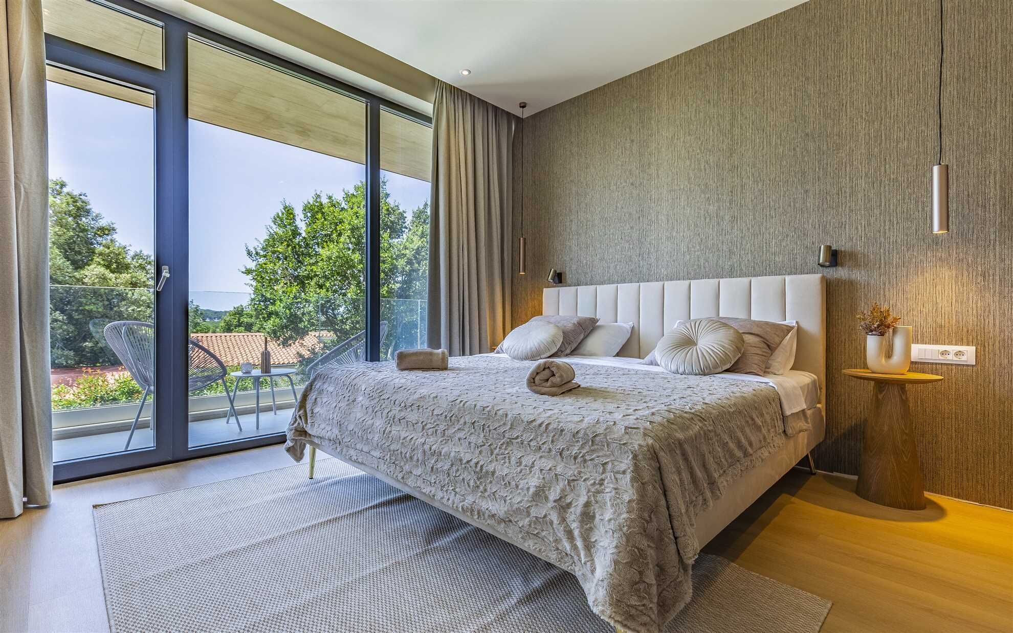 Ein modernes Schlafzimmer mit einem großen Bett, Blick durch die Glastür und einer Wand im Holzdesign.