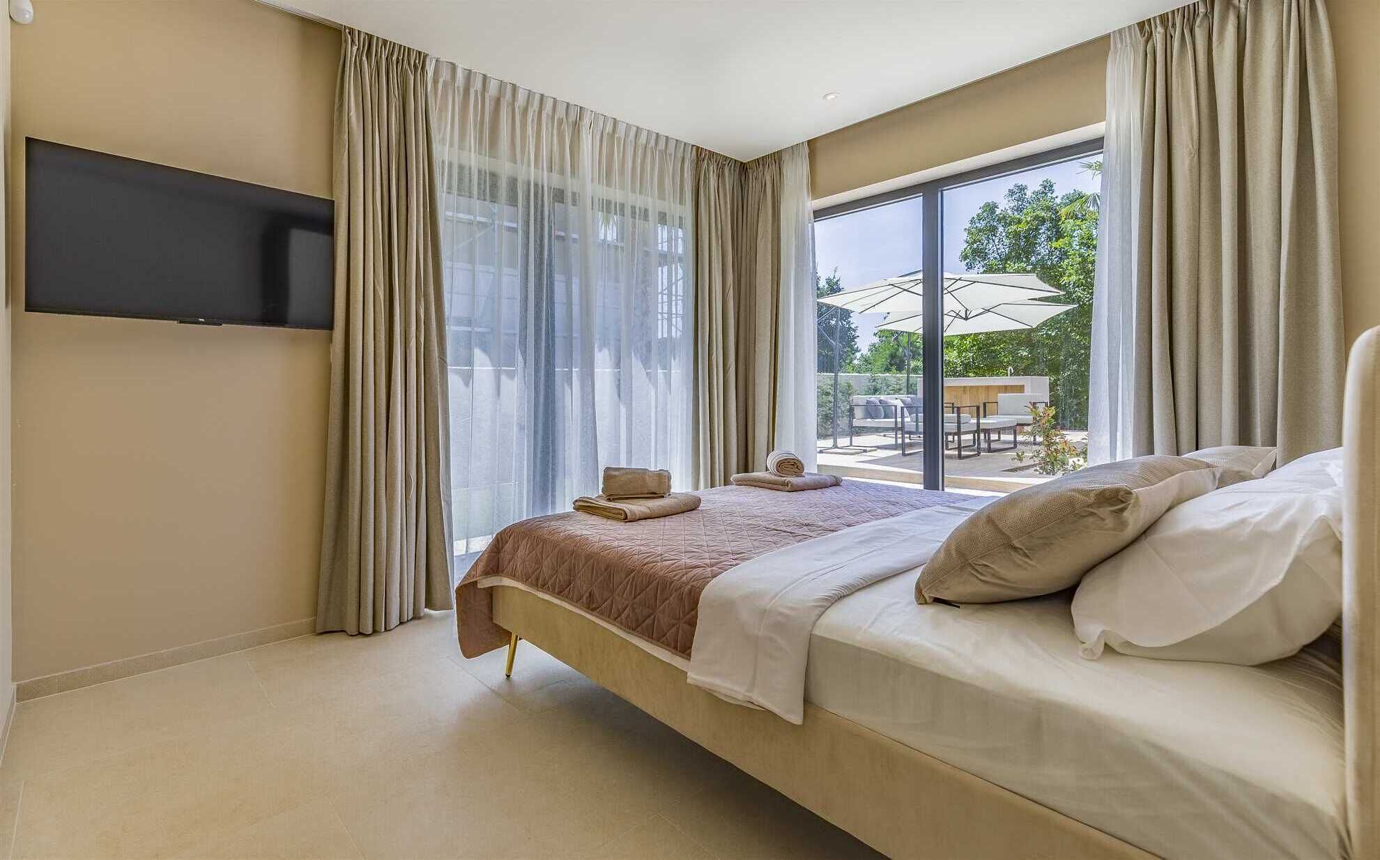 Et moderne hotelværelse med en stor seng, et fladskærms-tv ophængt på væggen og udsigt til en udendørs patio.