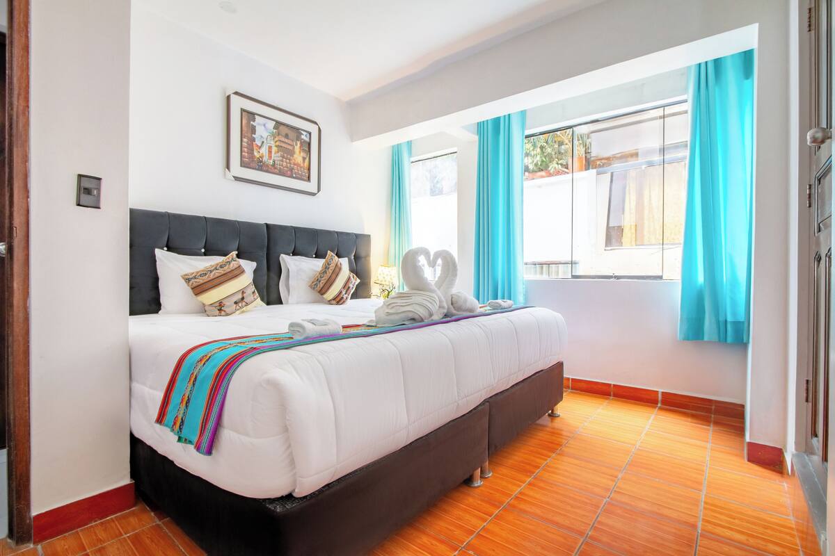 Habitación de hotel con una cama grande, cabecera, ventana con cortinas e imagen en la pared.