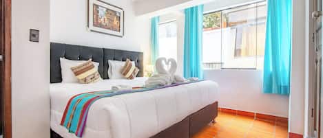 Habitación de hotel con una cama grande, cabecera, ventana con cortinas e imagen en la pared.