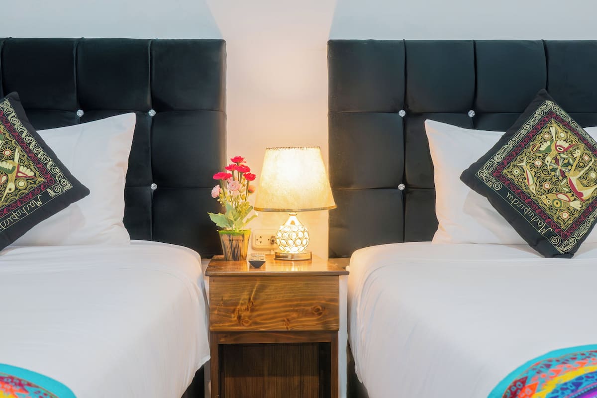 Una habitación de hotel con dos camas, una mesita de noche con lámpara y almohadas decorativas.